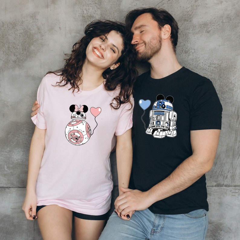 May include: A light pink t-shirt featuring a BB-8 droid design with Minnie Mouse ears and a pink heart balloon. A black t-shirt with an R2-D2 droid design with Mickey Mouse ears and a blue heart balloon.