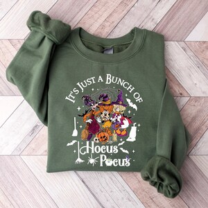 May include: Green sweatshirt with a white graphic of Mickey Mouse, Donald Duck, and Goofy dressed as witches. The graphic says "It's just a bunch of Hocus Pocus".