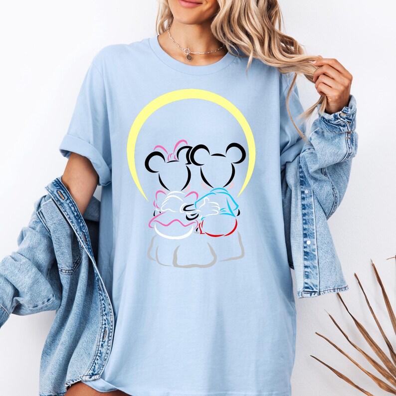 Puede incluir: Camiseta azul claro con un gr&aacute;fico de dos ratones de dibujos animados abraz&aacute;ndose, sobre un c&iacute;rculo amarillo. Los ratones est&aacute;n delineados en negro, con toques de rosa, azul y rojo. La camiseta tiene un corte holgado y mangas enrolladas.