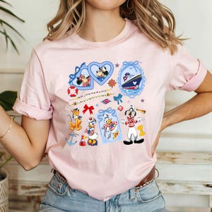 May include: Pink t-shirt with a nautical theme featuring Mickey Mouse, Minnie Mouse, Donald Duck, Goofy, and a cruise ship. The design includes hearts, stars, anchors, and ribbons.