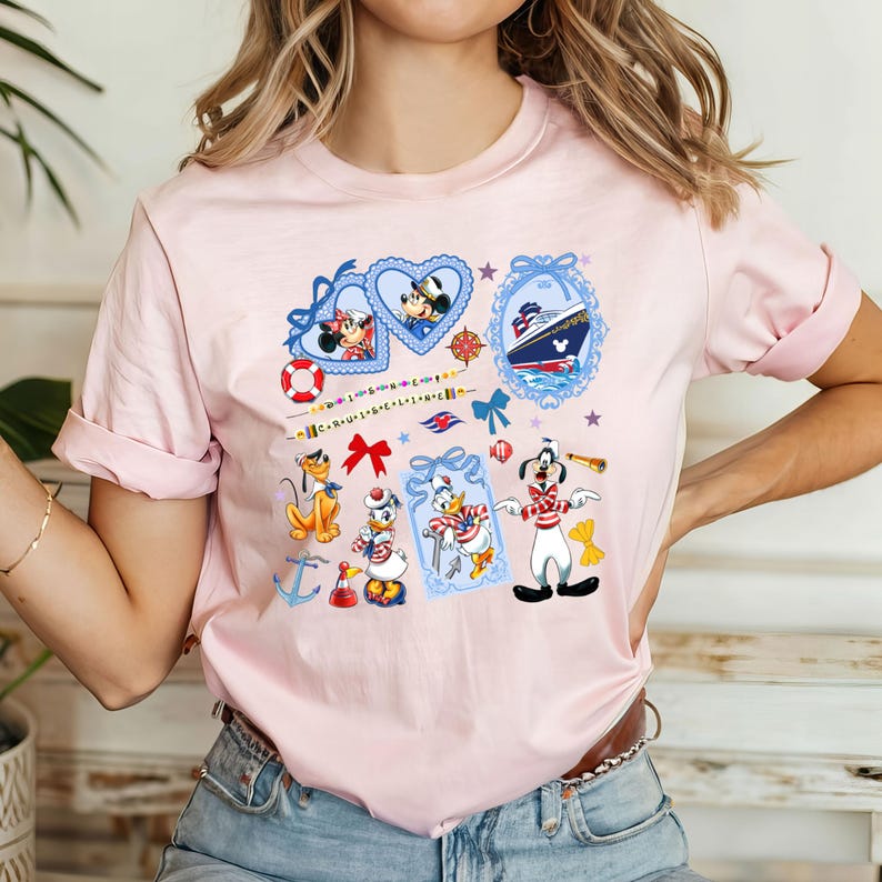 May include: Pink t-shirt with a nautical theme featuring Mickey Mouse, Minnie Mouse, Donald Duck, Goofy, and a cruise ship. The design includes hearts, stars, anchors, and ribbons.