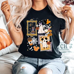 Puede incluir: Camiseta negra con un dise&ntilde;o de Halloween con Mickey y Minnie Mouse disfrazados de fantasmas, calabazas y un castillo embrujado. El dise&ntilde;o incluye la palabra "Magic" y una taza de caf&eacute;. La camiseta la lleva una persona.