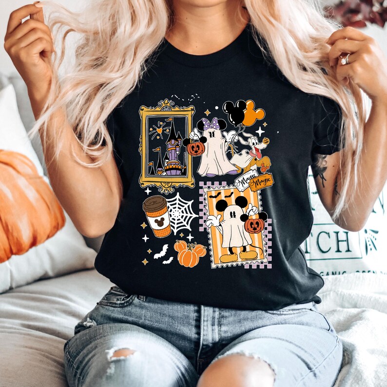 Puede incluir: Camiseta negra con un dise&ntilde;o de Halloween con Mickey y Minnie Mouse disfrazados de fantasmas, calabazas y un castillo embrujado. El dise&ntilde;o incluye la palabra "Magic" y una taza de caf&eacute;. La camiseta la lleva una persona.