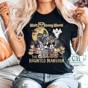 May include: Black t-shirt with a vintage-style graphic of Mickey Mouse and friends in front of the Haunted Mansion at Walt Disney World. The text "Walt Disney World" and "The Haunted Mansion" are printed on the shirt.