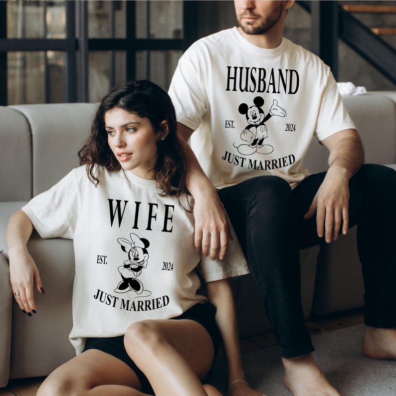 May include: A couple wearing matching white t-shirts with a Mickey Mouse and Minnie Mouse graphic. The shirts say "Husband Est. 2024 Just Married" and "Wife Est. 2024 Just Married".