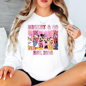 Puede incluir: Sudadera blanca con un gr&aacute;fico rosa y blanco de Mickey Mouse y sus amigos. El gr&aacute;fico dice "Mickey & Co. Est. 1928".