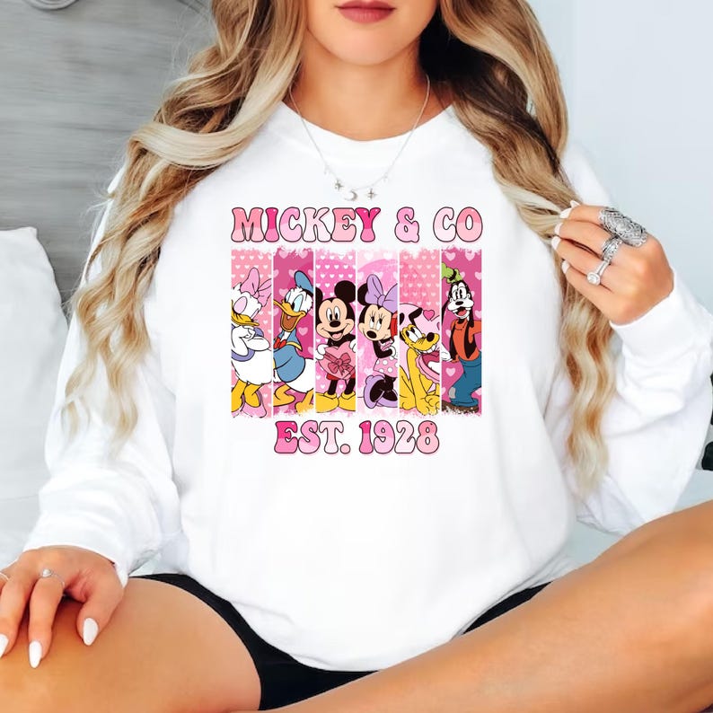 Puede incluir: Sudadera blanca con un gr&aacute;fico rosa y blanco de Mickey Mouse y sus amigos. El gr&aacute;fico dice "Mickey & Co. Est. 1928".