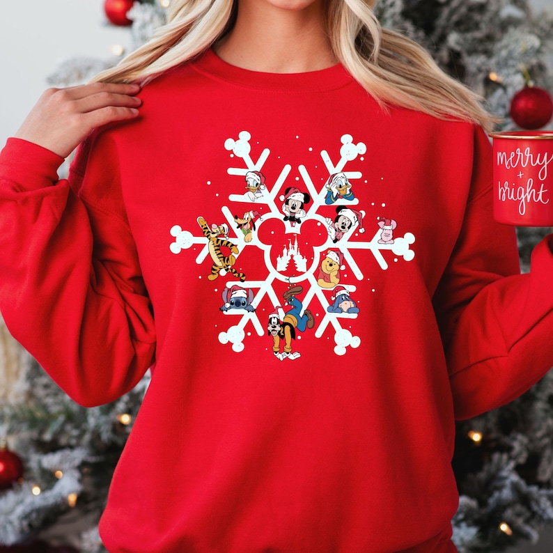 May include: Red Christmas sweatshirt featuring a snowflake design.  The snowflake incorporates various Disney characters, including Mickey Mouse, Minnie Mouse, Donald Duck, Goofy, Pluto, Stitch, Winnie the Pooh, and Tigger. The characters are depicted in a festive, cartoon style.  The sweatshirt is a comfortable, crewneck style, perfect for the holiday season.