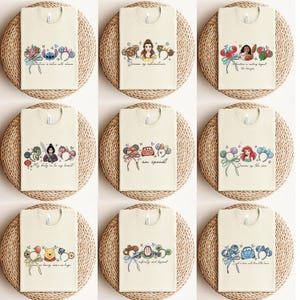 May include: Nine cream-coloured t-shirts with cartoon character designs. Each shirt features a different character or theme, including Stitch, Belle, Moana, Mulan, Cars, Ariel, Winnie the Pooh, Buzz Lightyear, and Lightning McQueen. Each shirt has a quote.