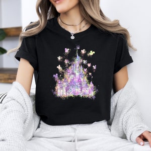 May include: A black t-shirt featuring a colourful watercolour illustration of Cinderella's castle with Mickey Mouse silhouettes surrounding it.