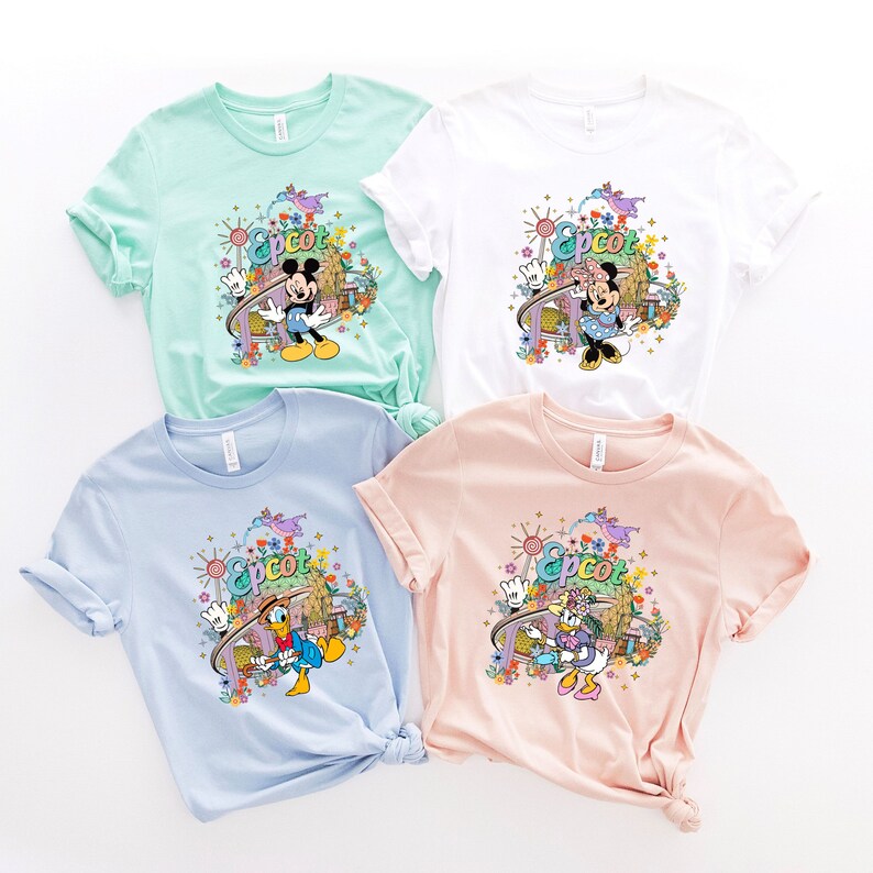 May include: Four t-shirts with different Disney characters and the word "Epcot" printed on them. The shirts are in different colors: light blue, light pink, white, and light green.