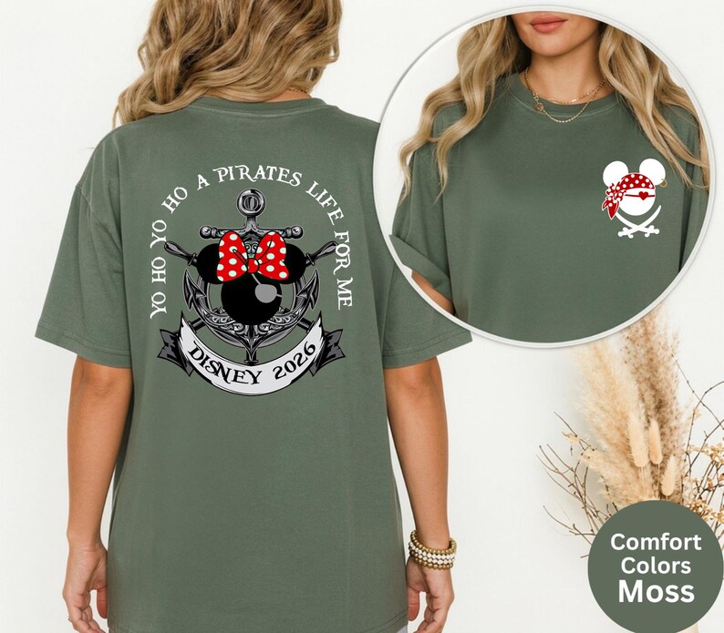 May include: Moss green t-shirt featuring a pirate-themed design. The back of the shirt displays an anchor with a Minnie Mouse head, a red polka-dot bow, and the text "Yo Ho Ho A Pirates Life For Me Disney 2026". The front has a smaller pirate Minnie Mouse design.