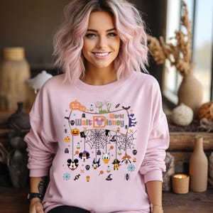 May include: Pink sweatshirt with a Halloween-themed design featuring Mickey Mouse and other Disney characters. The design includes a spiderweb, pumpkins, and the text "Walt Disney World".