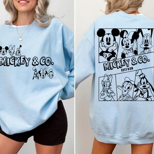 May include: Light blue sweatshirt with a black Mickey Mouse and friends graphic. The graphic includes Mickey Mouse, Minnie Mouse, Donald Duck, Goofy, and Pluto. The text "Mickey & Co. EST 1928" is printed below the graphic.