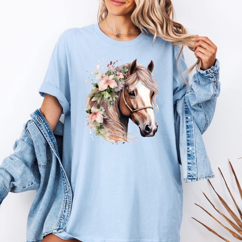 Peut inclure: T-shirt bleu clair avec une illustration &agrave; l'aquarelle d'une t&ecirc;te de cheval orn&eacute;e de fleurs roses et de verdure. Le cheval porte un licol marron et une crini&egrave;re flottante. Le t-shirt est de coupe d&eacute;contract&eacute;e.