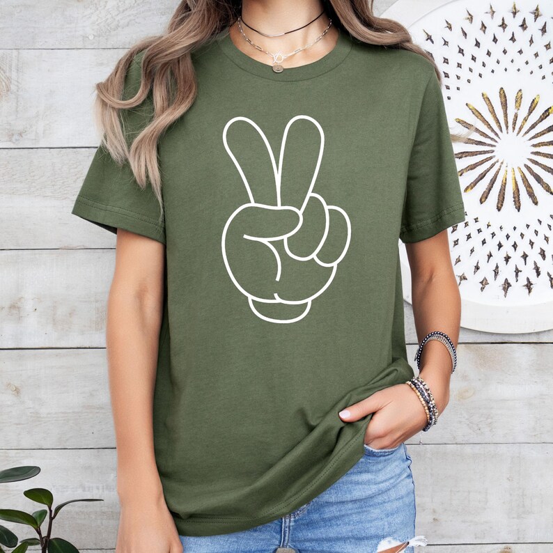 K&ouml;nnte beinhalten: Olivgr&uuml;nes T-Shirt mit wei&szlig;em Umriss einer Hand, die das Friedenszeichen zeigt. Das kurz&auml;rmelige Shirt ist aus einem weichen Material gefertigt. Die Grafik ist mittig auf der Vorderseite des Shirts angebracht.