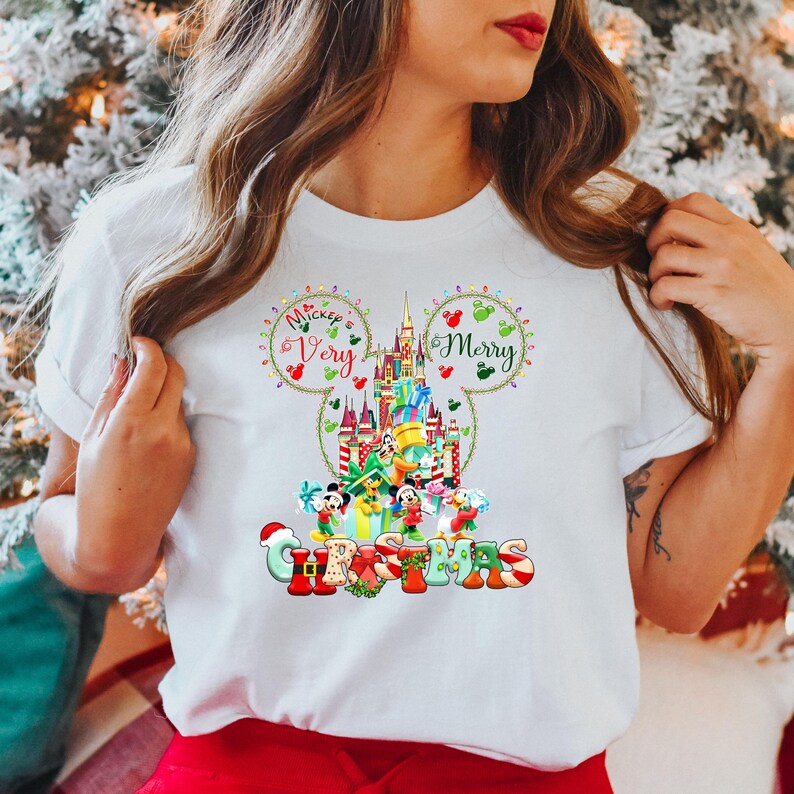 May include: White t-shirt featuring a colourful graphic of Mickey Mouse's ears with the text "Mickey's Very Merry Christmas" and a depiction of Cinderella's castle with Mickey Mouse and other Disney characters.