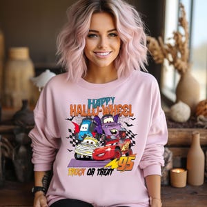 Może przedstawiać: R&oacute;żowa bluza z nadrukiem kresk&oacute;wek samochod&oacute;w przebranych na Halloween. Tekst na bluzce brzmi "Happy Hallo-Wheel Trick or Treat".