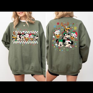 Puede incluir: Sudadera verde de Navidad con un dise&ntilde;o festivo que presenta a Mickey Mouse, Minnie Mouse, Donald Duck, Goofy y Pluto con gorros de Pap&aacute; Noel y rodeados de luces navide&ntilde;as. La sudadera tiene un patr&oacute;n a cuadros en la parte delantera y un dise&ntilde;o completo en la parte posterior.