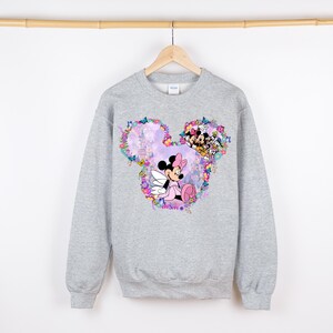 May include: A gray sweatshirt with a floral design featuring Mickey Mouse and Minnie Mouse. The design is in the shape of Mickey Mouse's ears.