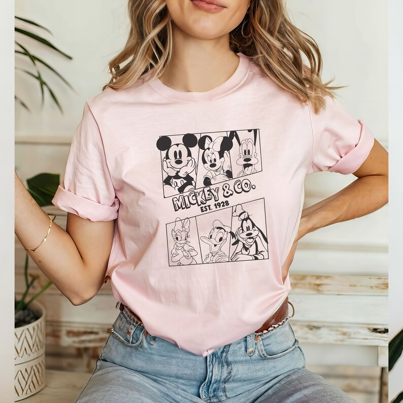K&ouml;nnte beinhalten: Ein pinkfarbenes T-Shirt mit einem schwarz-wei&szlig;en Grafikdruck von Mickey Mouse, Minnie Mouse, Donald Duck und Goofy. Die Grafik enth&auml;lt den Text "Mickey & Co. Est. 1928".