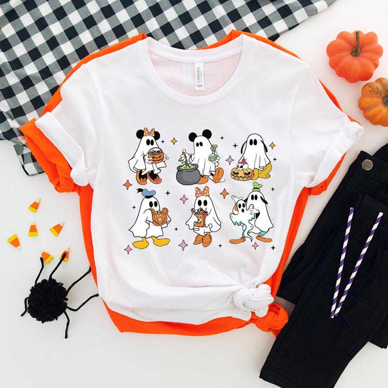 May include: White t-shirt featuring a graphic of Disney characters dressed as ghosts for Halloween. The characters include Mickey Mouse, Minnie Mouse, Donald Duck, Goofy, and Pluto.