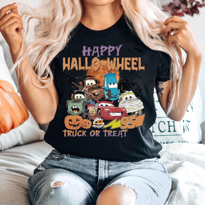 May include: A black t-shirt with a graphic of cartoon cars dressed up for Halloween. The text "Happy Hallo-Wheel Truck or Treat" is printed on the shirt.