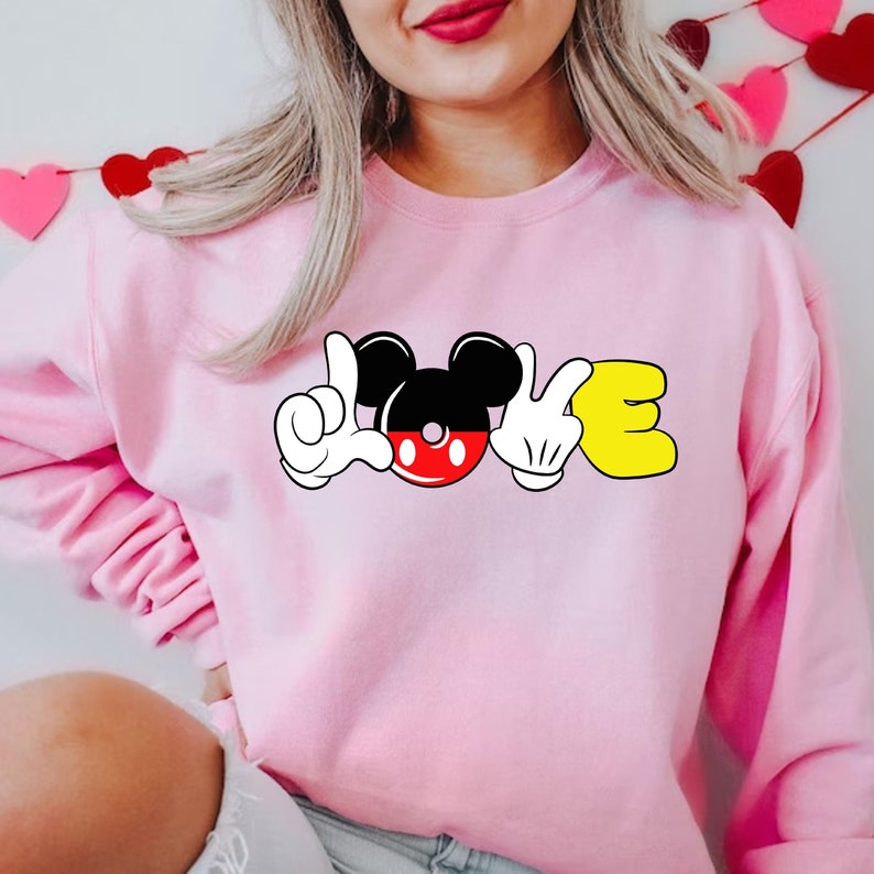 May include: Pink sweatshirt with a Mickey Mouse head and hands spelling out "LOVE" in a cartoon style.