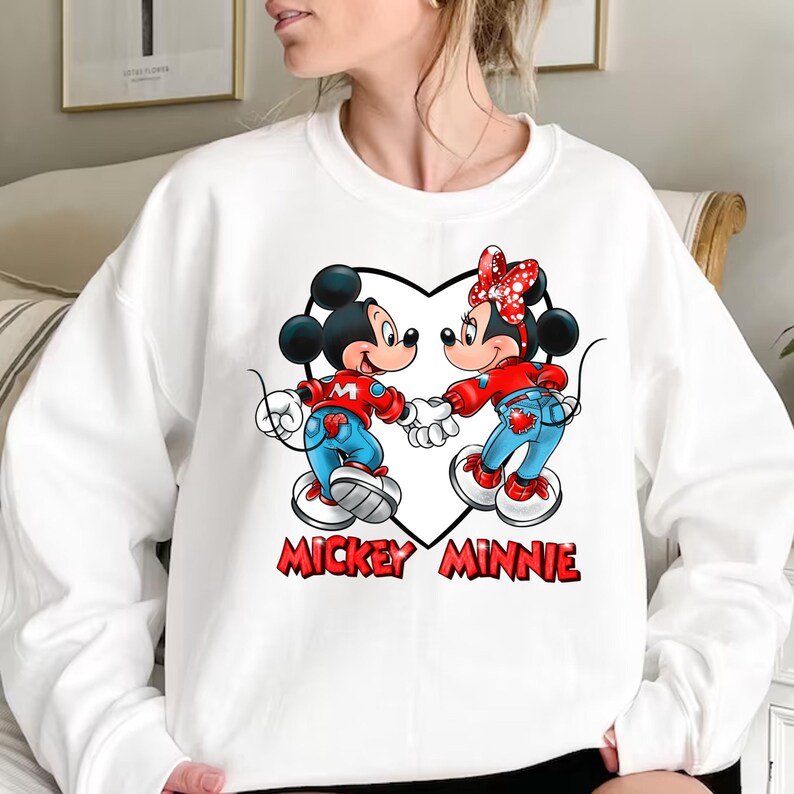 May include: White sweatshirt with a graphic of Mickey Mouse and Minnie Mouse holding hands inside a heart. The text "Mickey Minnie" is printed below the graphic.