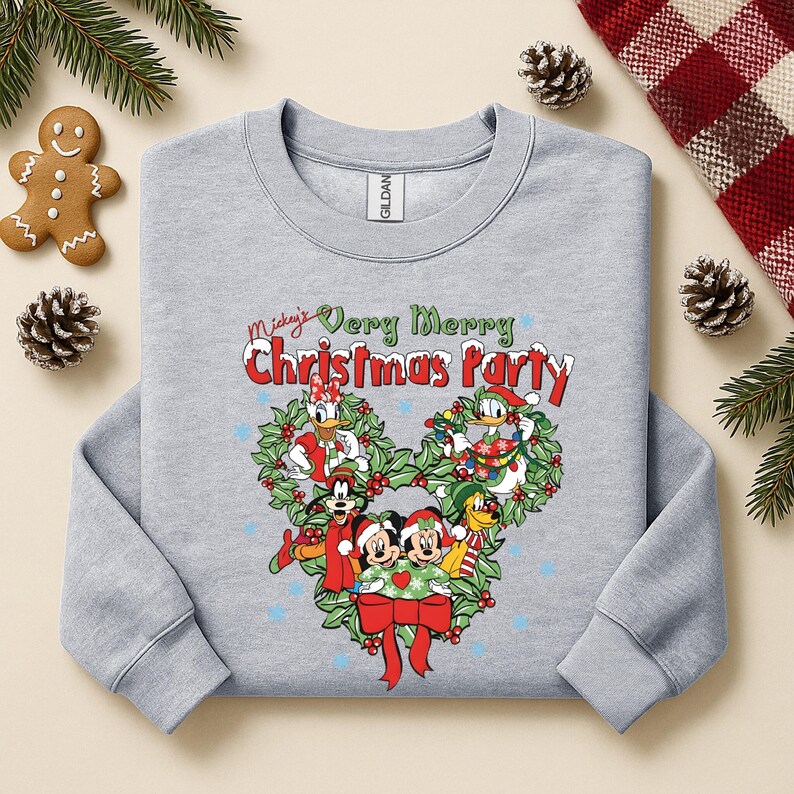 Op de afbeelding: Een lichtgrijs sweatshirt met een feestelijk ontwerp met Mickey Mouse en vrienden. De afbeelding bevat de tekst "Mickey's Very Merry Christmas Party" en is omgeven door een krans. Blauwe sterren zijn verspreid rond het ontwerp.