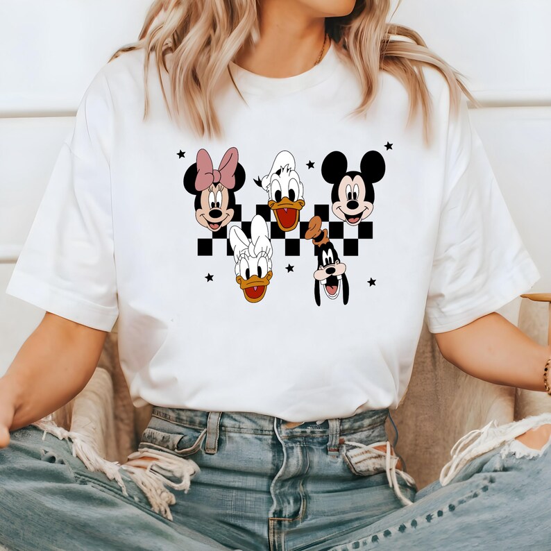 Puede incluir: Camiseta blanca con un patr&oacute;n de cuadros blanco y negro e im&aacute;genes de Mickey Mouse, Minnie Mouse, Donald Duck, Daisy Duck y Goofy.