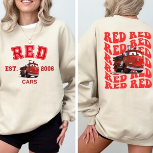 May include: A cream colored sweatshirt with a red graphic of a fire truck and the text "RED EST. 2006 CARS". The back of the sweatshirt has the word "RED" repeated in a retro style.