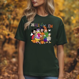 May include: Dark green t-shirt featuring a Halloween design with cartoon characters. The word "HALLOWEEN" is displayed in colorful letters above the characters. The characters include Mickey Mouse, Minnie Mouse, Donald Duck, and Goofy.