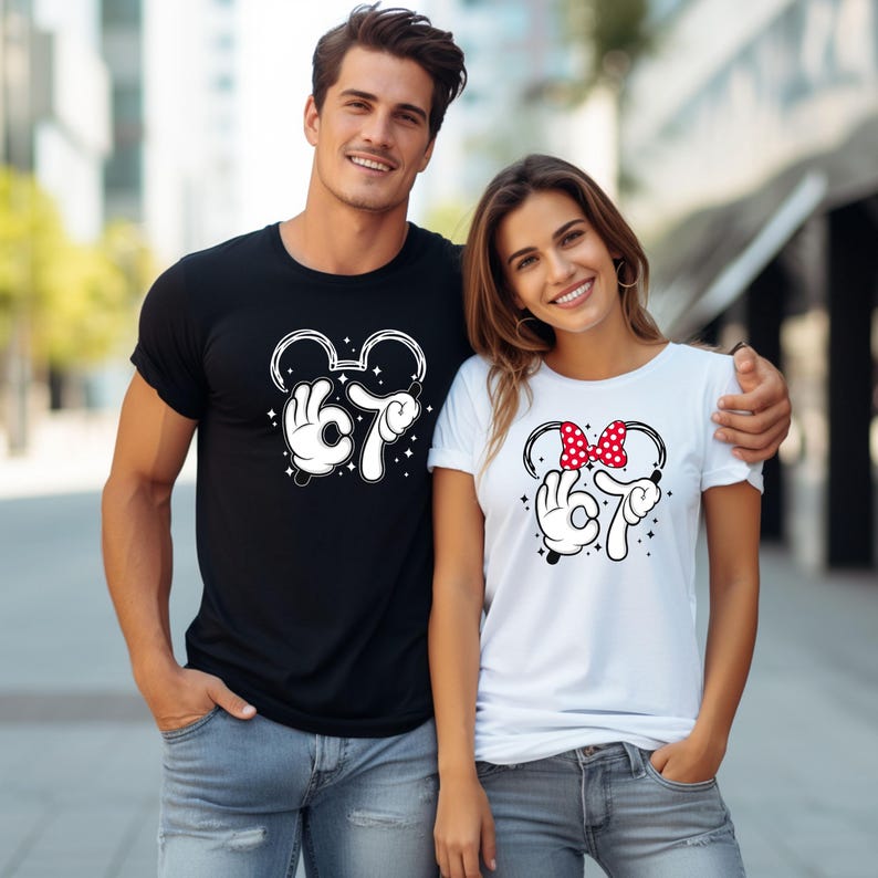 K&ouml;nnte beinhalten: Schwarzes T-Shirt mit wei&szlig;em Mickey Mouse-Design, einschlie&szlig;lich der Zahl 67 und einer Handgeste. Ein wei&szlig;es T-Shirt mit einem Minnie Mouse-Design, einschlie&szlig;lich der Zahl 67 und einer Handgeste. Das Minnie Mouse-Design enth&auml;lt eine rote Schleife mit Punkten.