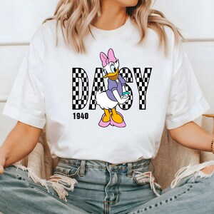 May include: White t-shirt with a black and white checkered design that spells out "DAISY" with a cartoon image of Daisy Duck in the center. The year "1940" is printed below the design.