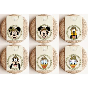 May include: Six beige t-shirts with different Disney characters wearing safari hats. The characters are Mickey Mouse, Minnie Mouse, Donald Duck, Goofy, Pluto, and Daisy Duck.