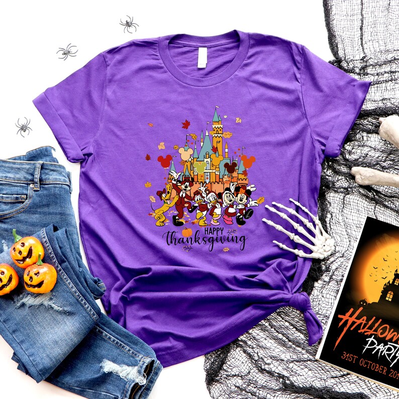 May include: Purple t-shirt with a graphic of Mickey Mouse and friends in front of the Cinderella Castle with the text "Happy Thanksgiving".