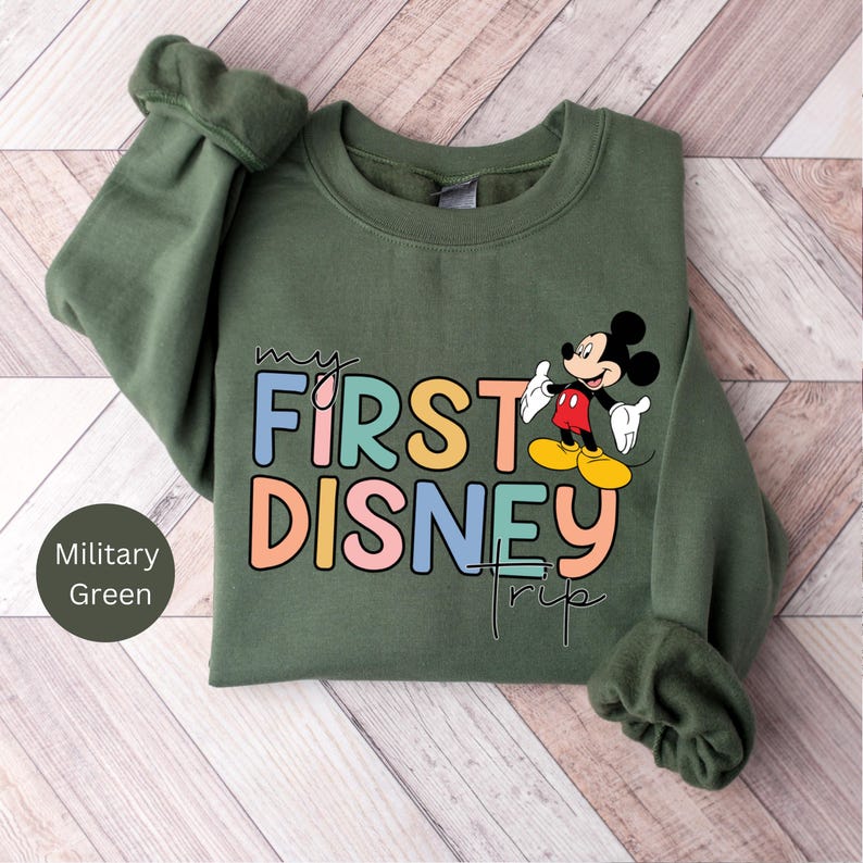 May include: A green sweatshirt with the text "my first disney trip" in colorful letters and a cartoon image of Mickey Mouse.