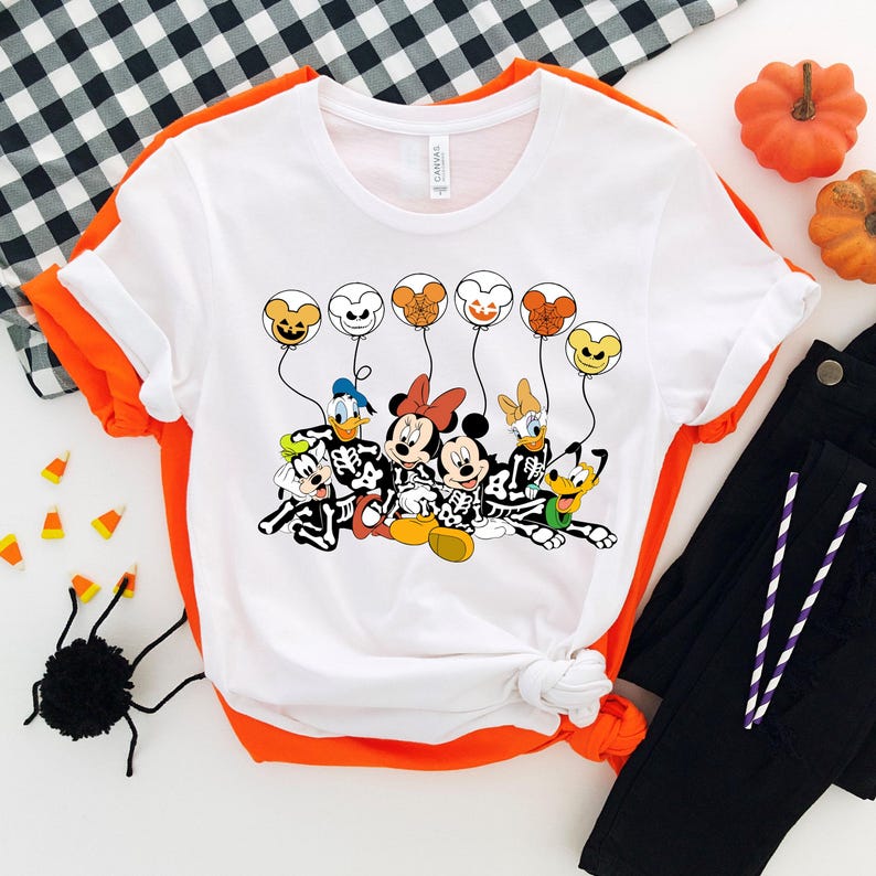 May include: White t-shirt with a graphic of Mickey Mouse, Minnie Mouse, Donald Duck, Goofy, and Pluto dressed as skeletons holding balloons with Halloween-themed designs.