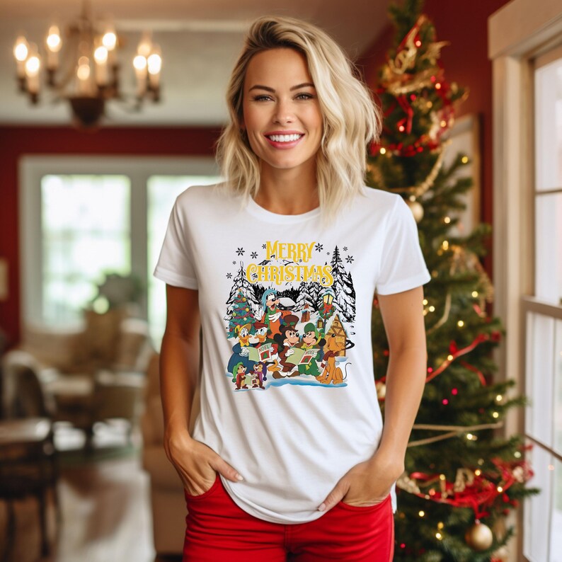May include: White t-shirt with a Christmas-themed graphic featuring Mickey Mouse and other Disney characters. The graphic includes the text "Merry Christmas".