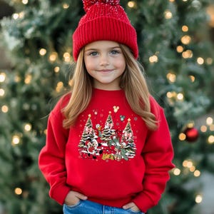 May include: A red Christmas sweater with a festive design featuring Mickey Mouse, Minnie Mouse, Donald Duck, and Goofy. The characters are standing in front of Christmas trees with presents and snowflakes.