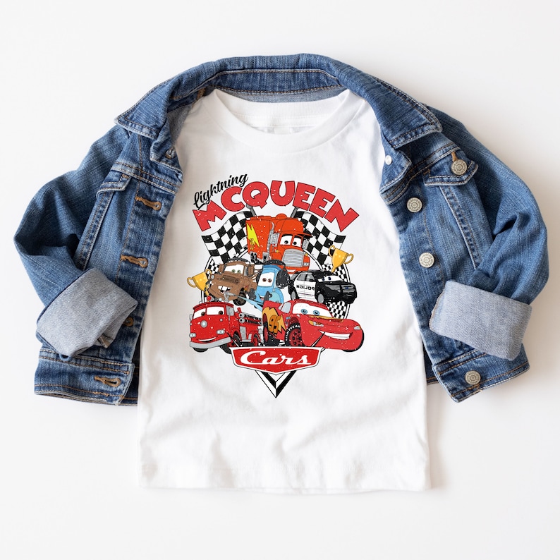 May include: White t-shirt with a graphic of Lightning McQueen and other Cars characters. The graphic features a checkered flag background and the text "Lightning McQueen" and "Cars".