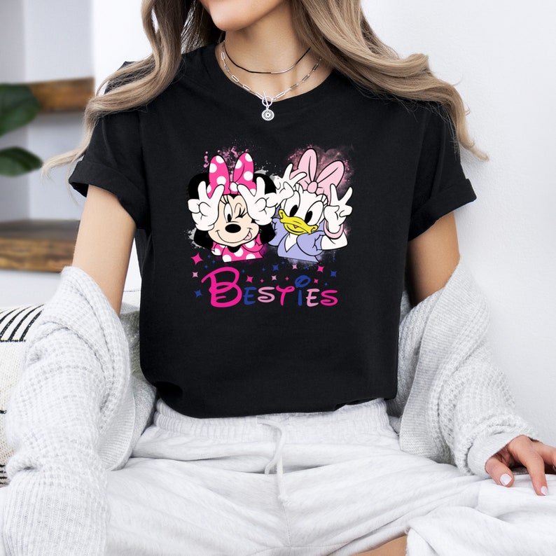 May include: Black t-shirt with a graphic of Minnie Mouse and Daisy Duck with the word "Besties" printed below them.