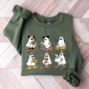 May include: A green sweatshirt with a Halloween-themed design featuring cartoon ghosts dressed as Mickey Mouse, Minnie Mouse, Donald Duck, and Goofy. The ghosts are holding pumpkins, a cauldron, and sweets.