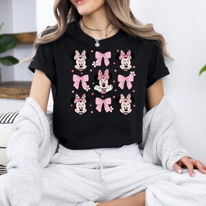May include: Black t-shirt with a repeated pattern of Minnie Mouse heads and pink bows.