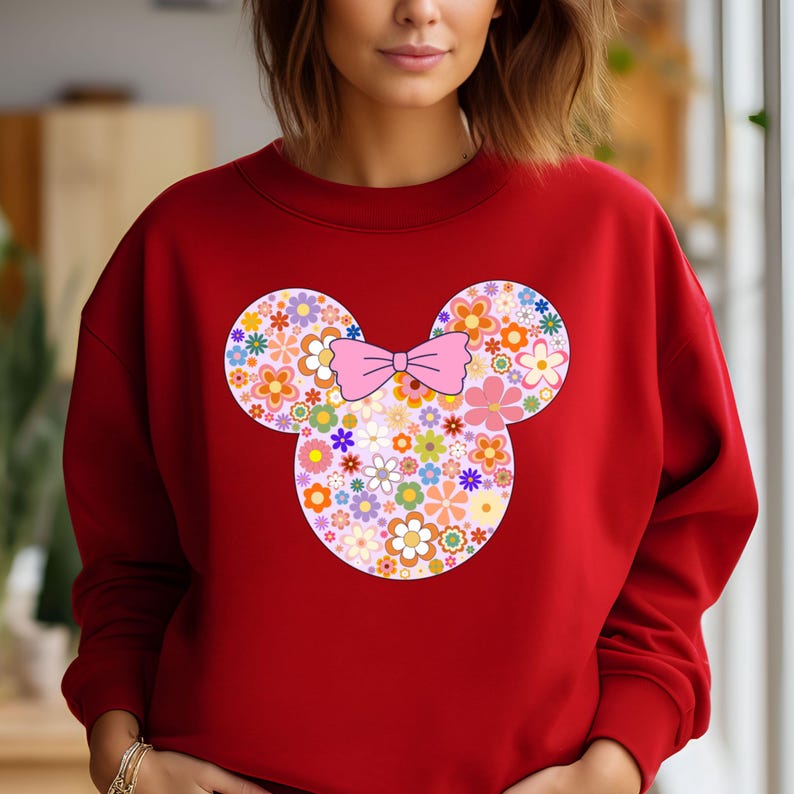 May include: A red sweatshirt featuring a floral Mickey Mouse design. The design includes a pink bow and the mouse's iconic ears filled with colorful flowers. The sweatshirt is a solid red color.