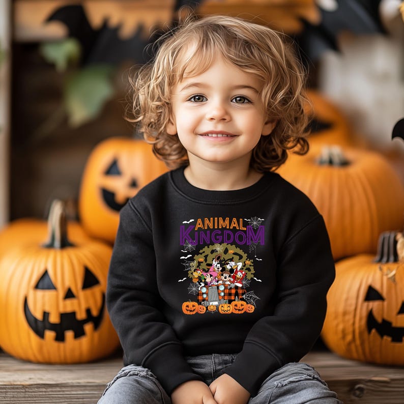 May include: A child in a black sweatshirt with the words "ANIMAL KINGDOM" and a cartoon graphic. The background includes carved pumpkins and Halloween decorations, creating a festive atmosphere.