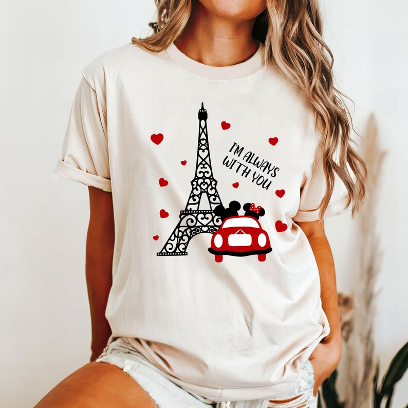 May include: A white t-shirt with a black graphic of the Eiffel Tower, Mickey Mouse and Minnie Mouse in a red car, and the text "I'm Always With You". There are red hearts scattered around the graphic.