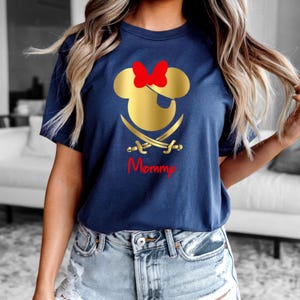 May include: A navy blue t-shirt with a gold Mickey Mouse head with a red bow and an eye patch. Two gold swords are crossed behind the head. The text "Mommy" is written in red below the head.