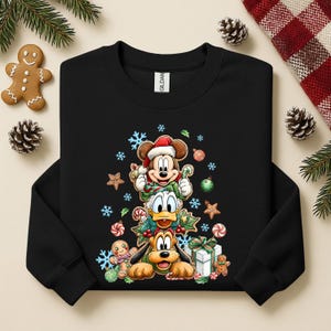 Peut inclure: Sweat-shirt noir avec Mickey Mouse, Donald Duck et Pluto empil&eacute;s, tous v&ecirc;tus pour No&euml;l. Le motif comprend des flocons de neige, des cannes en sucre et des bonhommes en pain d'&eacute;pices. V&ecirc;tements de vacances festifs.